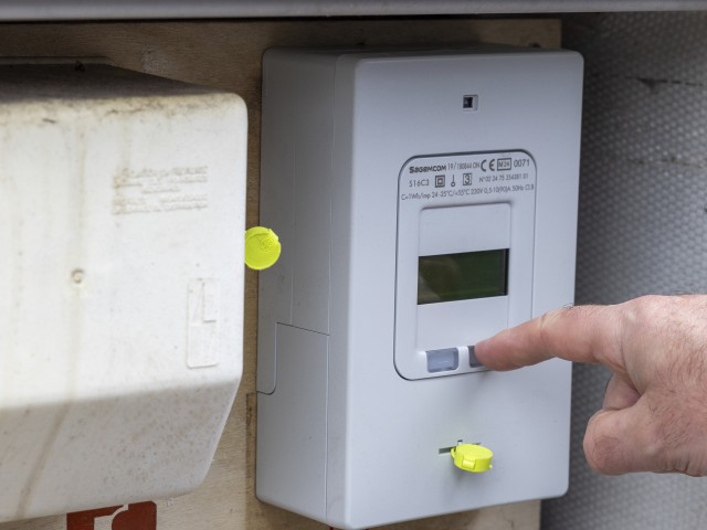 Une personne interagit avec un compteur électrique triphasé installé dans un boîtier extérieur, en appuyant sur un bouton du tableau.